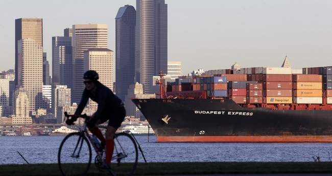 A bicyclist rides in view of a loaded container ship anchored in Elliott Bay near downtown Seattle in 2014. With a second major carrier all but pulling out of the Port of Portland, there's concern that business will move to Seattle, increasing costs. (AP Photo)