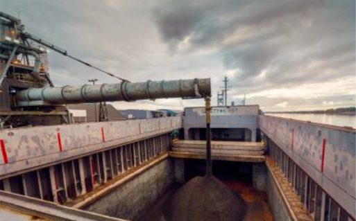 Copper concentrate loading into ship hold from covered storage warehouse.