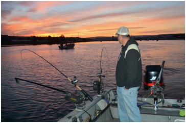 Boat angler watches pole for a strike while salmon fishing.