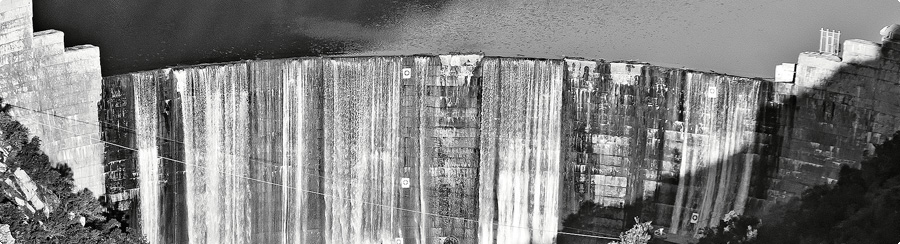 Stark contrast between a dam wall and reservoir's edge; artifice impinging nature's natural movement