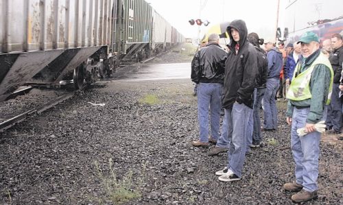 Participants in the Washington Association of Wheat Growers legislative tour watch in the rain as a train goes by the afternoon of May 23 on a road crossing near Medical Lake, Wash. Wheat growers and state representatives say the poor condition of the state-owned railroad needs to be addressed. (Matthew Weaver photo)
